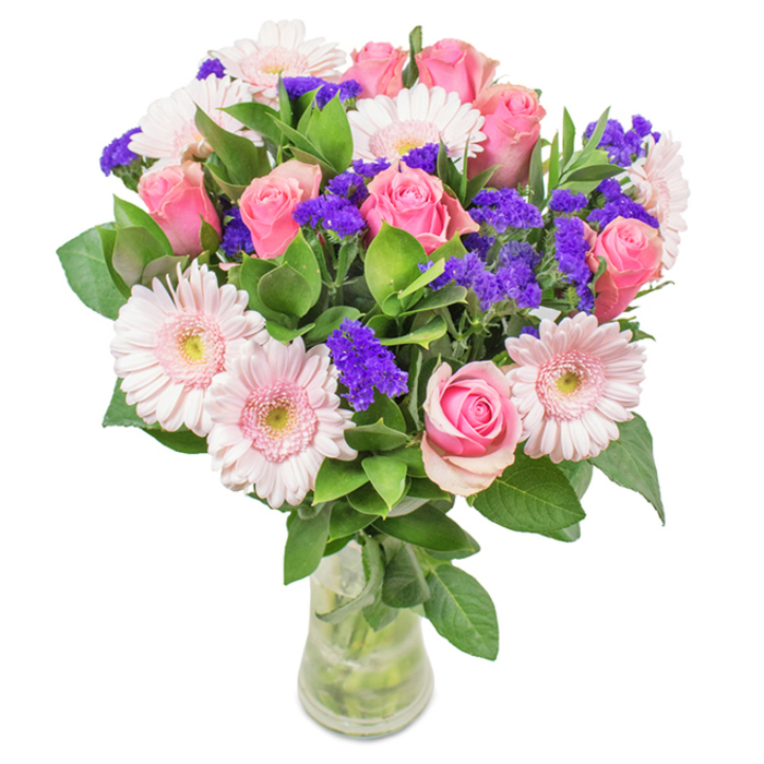 A radiant, thoughtfully composed bouquet sits elegantly in a crystal-clear vase, photographed against a soft white background-embodying Alperton's affinity for understated yet joyful beauty. Pink roses, numbering around eight, reveal their classic spiral shapes, each bloom at various stages of opening, petals plush and inviting. Intertwined among them, five or six delicate pink gerbera daisies display wide, sunlike heads with captivating pale faces and creamy-to-white centers, creating an inviting contrast. Accentuating the arrangement are vivid purple sprigs of statice or limonium, their fine, textural blossoms catching the eye with dashes of deeper color, giving depth and rhythm to the display. Glossy, abundant green foliage-reminiscent of the leafy canopies on Alperton Lane-wraps the base and supports the vibrant blooms above. Visible through the pristine vase, every stem stands tall in clear water, underscoring the bouquet's freshness and quality. This arrangement, with its harmonious blend of pinks and purples, is perfect for special occasions like Mother's Day, birthdays, or as an elegant centrepiece in a home near One Tree Hill Recreation Ground. Designed by passionate Alperton florists, it expresses joy, affection, and a refined sense of celebration.